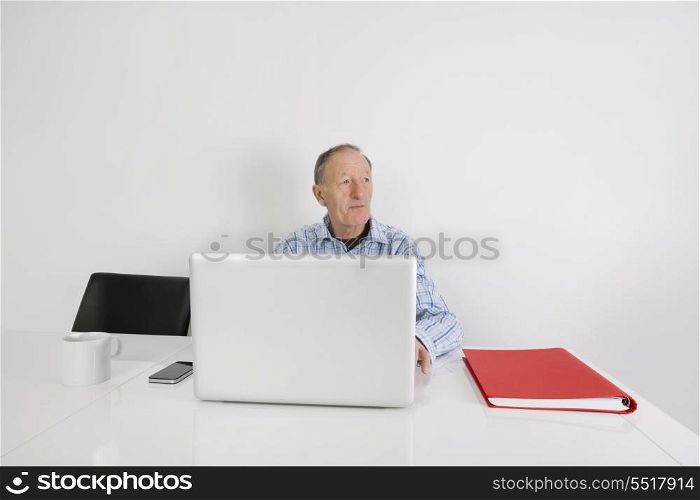 Thoughtful senior businessman using laptop at office desk