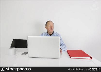 Thoughtful senior businessman using laptop at office desk