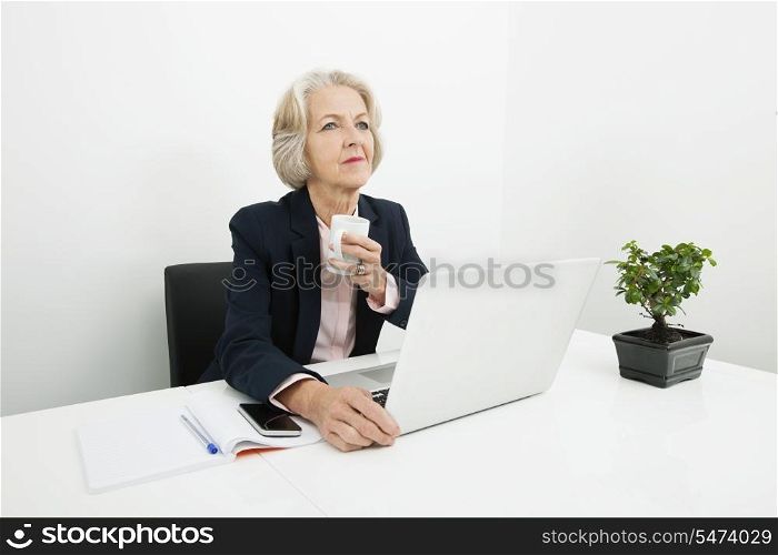 Thoughtful senior businesswoman having coffee at desk in office