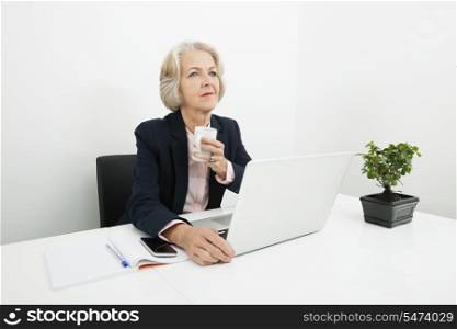 Thoughtful senior businesswoman having coffee at desk in office