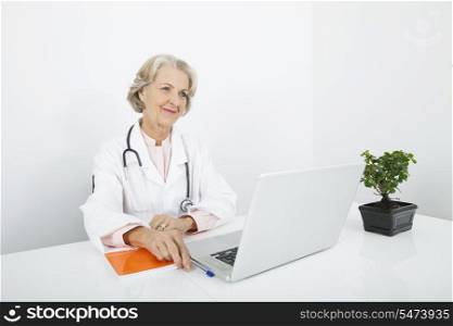 Thoughtful senior female doctor with laptop at desk in clinic