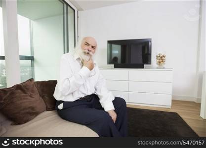 Thoughtful senior man sitting on sofa in living room