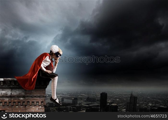 Thoughtful superkid. Cute supergirl of school age sitting on top of building