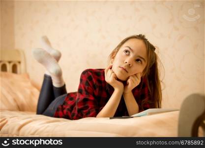 Thoughtful teenage girl lying on bed at bedroom