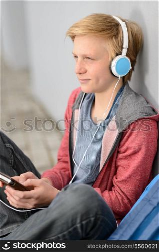 Thoughtful teenage student with headphones listening to music sitting outside