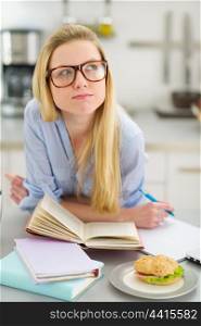 Thoughtful teenager girl studying in kitchen