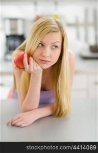 Thoughtful teenager girl with apple in kitchen
