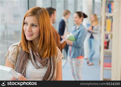 Thoughtful university student with classmates in background at library