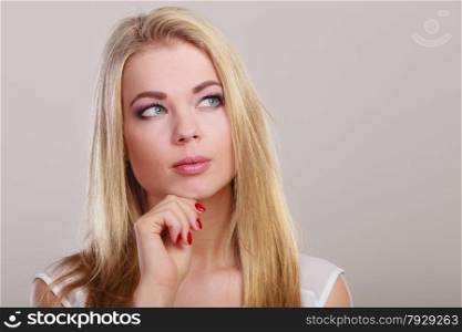Thoughtful woman face. Attractive blonde girl thinking on gray background