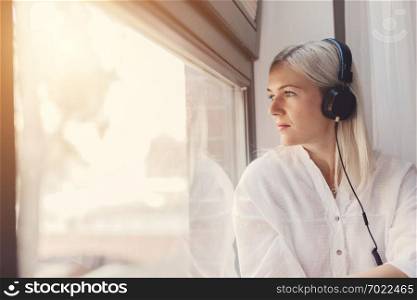 Thoughtful woman listening to music, looking through the window. Leisure, relax. Nostalgia.. Woman listening to music, looking through the window.
