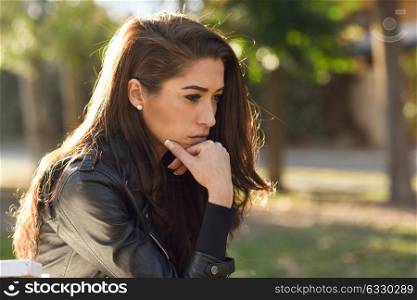 Thoughtful woman sitting alone outdoors. Girl worried in an urban park