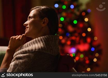 Thoughtful woman sitting chair in front of Christmas tree