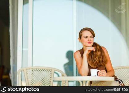 Thoughtful woman sitting on terrace and having cup of coffee&#xA;