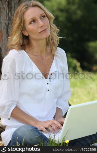 Thoughtful woman typing at a laptop computer in a garden