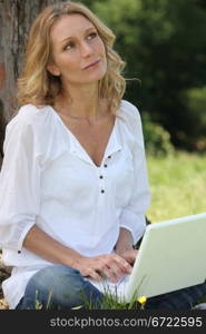 Thoughtful woman typing at a laptop computer in a garden