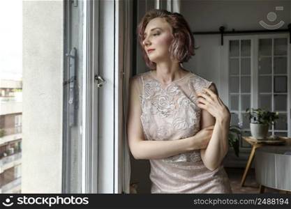 Thoughtful woman wearing a elegant dress looking standing by window