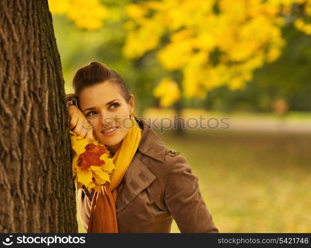 Thoughtful woman with fallen leaves leaning against tree