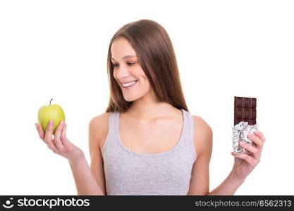 Thoughtful young blonde woman hesitating between a fruit and chocolate, isolated over white background