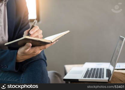 Thoughtful young business man in casual shirt holding note pad in a notebook on a wooden table with pen working in a cafe.