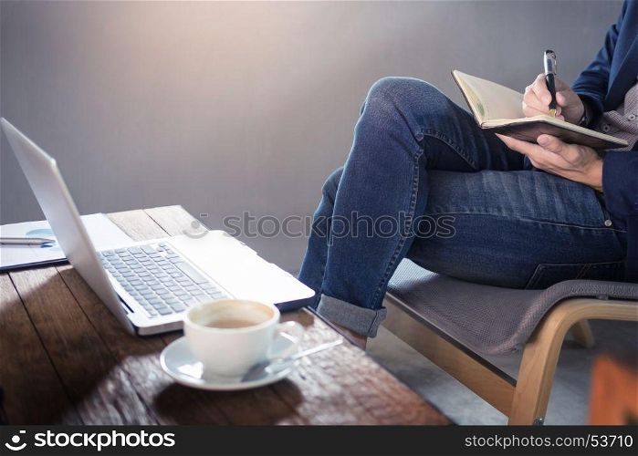 Thoughtful young business man in casual shirt holding note pad in a notebook on a wooden table with pen working in a cafe.
