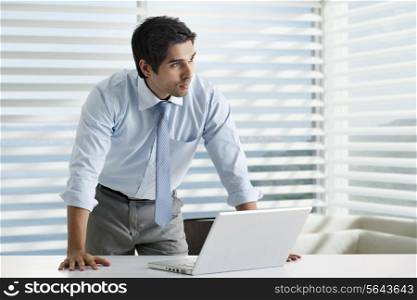 Thoughtful young business man standing at his desk