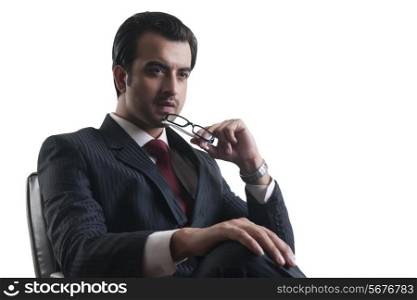 Thoughtful young businessman holding glasses against white background
