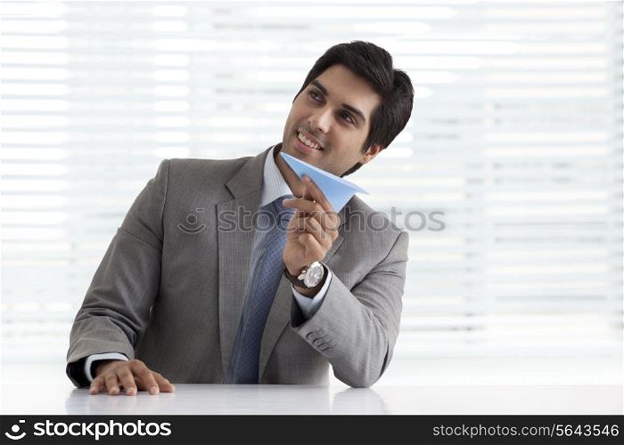 Thoughtful young businessman holding paper plane at his desk