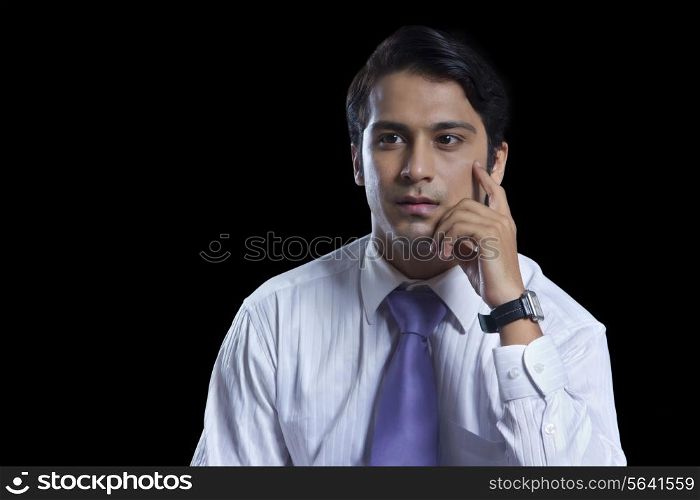 Thoughtful young businessman with hand on chin over black background