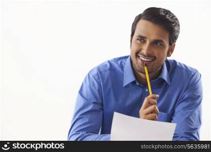 Thoughtful young businessman with pencil and paper over white background