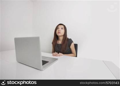 Thoughtful young businesswoman looking up with laptop at office desk
