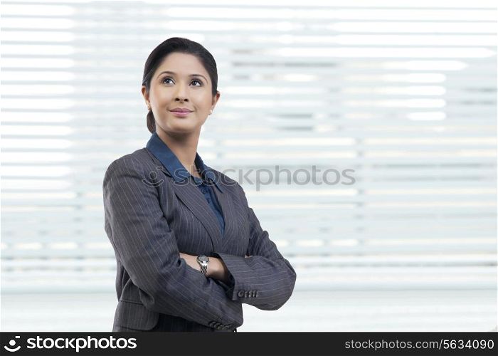 Thoughtful young businesswoman with arms crossed in office