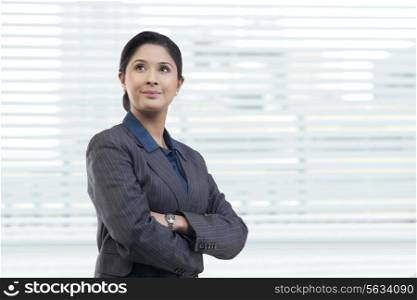 Thoughtful young businesswoman with arms crossed in office