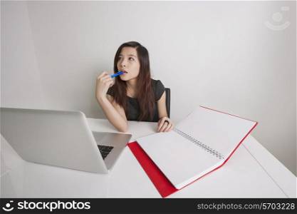 Thoughtful young businesswoman with diary and laptop at office desk