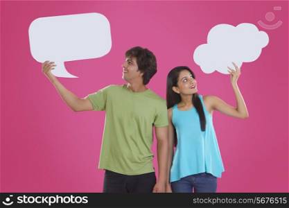 Thoughtful young couple holding communication bubbles against pink background