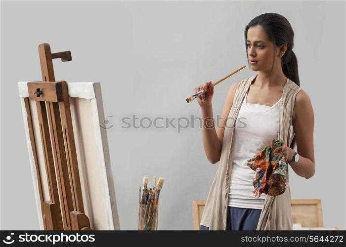Thoughtful young female artist looking at painting
