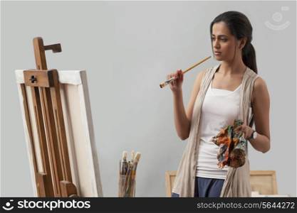 Thoughtful young female artist looking at painting
