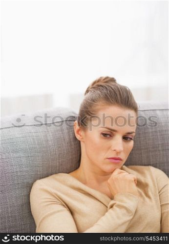 Thoughtful young housewife sitting on couch