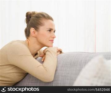 Thoughtful young housewife sitting on sofa looking on copy space