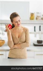 Thoughtful young housewife with apple in modern kitchen