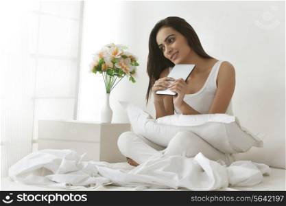 Thoughtful young Indian woman holding digital tablet on bed