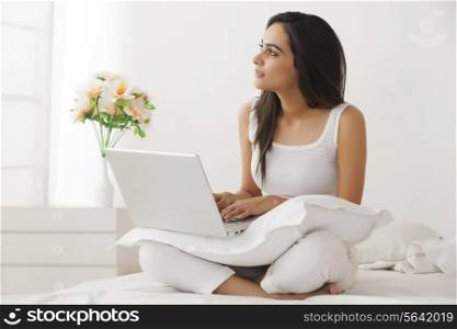 Thoughtful young Indian woman using laptop on bed