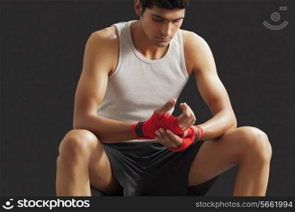Thoughtful young male boxer sitting against black background