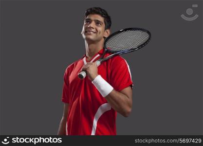 Thoughtful young man holding tennis racket isolated over black background