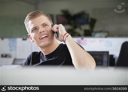 Thoughtful young man looking away while using cell phone at office