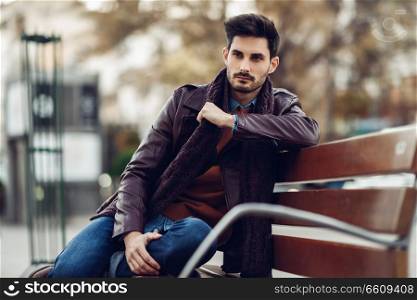 Thoughtful young man sitting on an urban bench. Attractive guy with modern hairstyle with lost look in the street.
