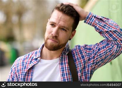 Thoughtful young man standing in urban background. Lifestyle con. Thoughtful young man standing in urban background. Guy looking away wearing casual clothes. Lifestyle concept.