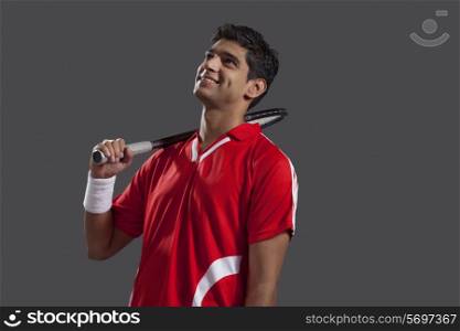 Thoughtful young man with tennis racket isolated over black background