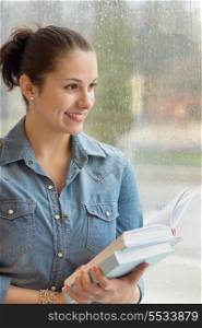 Thoughtful young student holding books by wet window