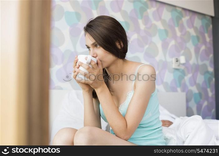Thoughtful young woman drinking coffee in bedroom