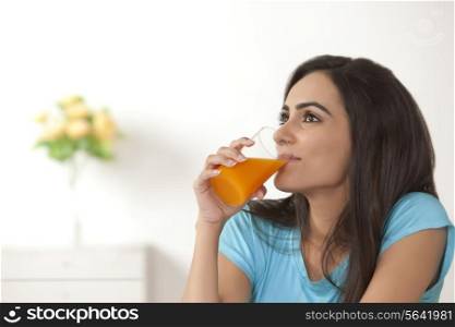 Thoughtful young woman drinking orange juice at home